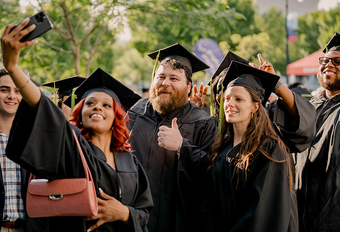 graduating students in regalia take a selfie group photo