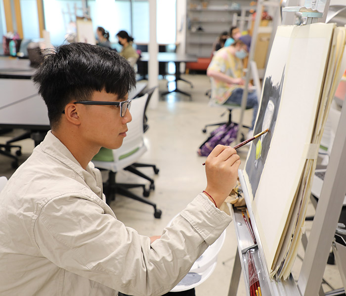 Student in fine arts class paints on a pad mounted on an easel
