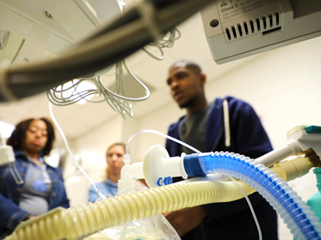 perspective from behind respiratory machine with plastic tubing and three out of focus students in background