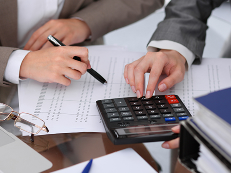 Two business people use a calculator on top of a sheet of numbers.