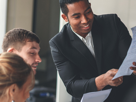 A businessperson holds a document in front of a group during a meeting.