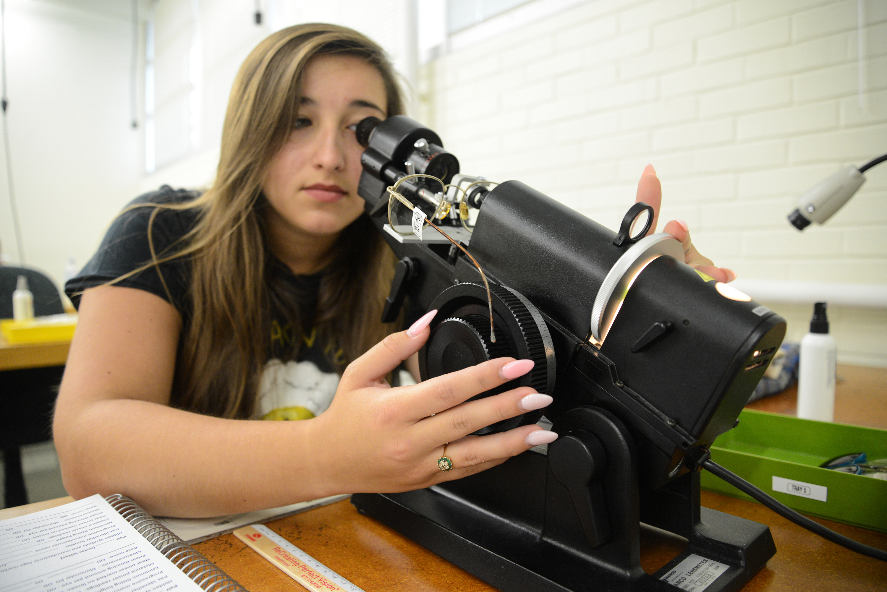 student looking closely into optical equipment to adjust glasses