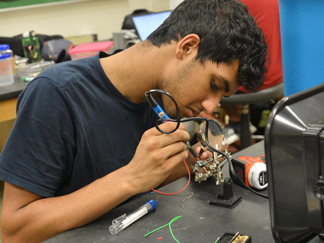 A student in the Associate in Engineering program at Durham Tech uses a tool to work on a metal trinket in class.