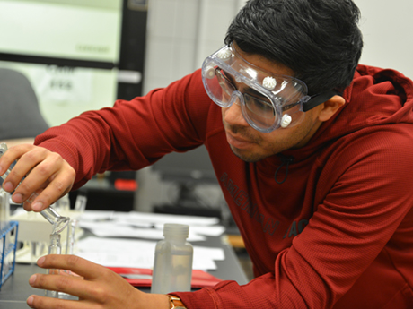 A male student in the Associate in Science program pours liquid into a beaker in a chemistry classroom.