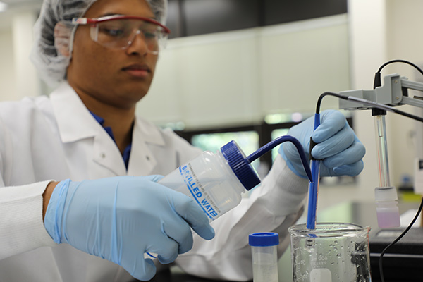 biowork student wearing a gown and mask working with lab equipment