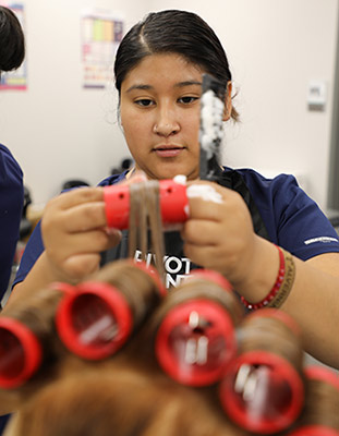 A student practices a roller set on a dummy head