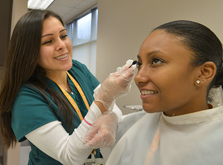 A student applies mascara to a clinic patron