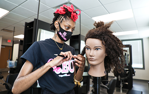 student practices styling a dummy head of natural hair