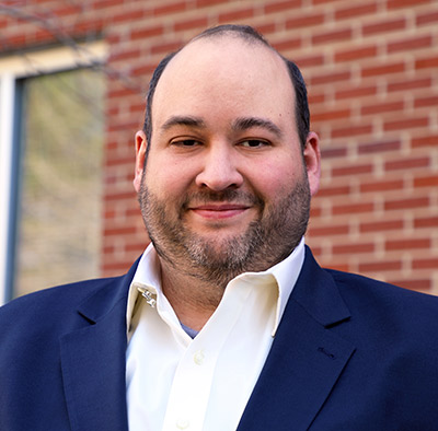 Chris McDuff poses in front of a brick building on campus