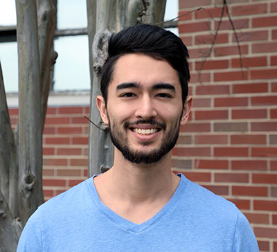 Joseph poses in front of a brick building on campus