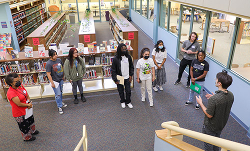 a small group of students listen to a librarian in the library