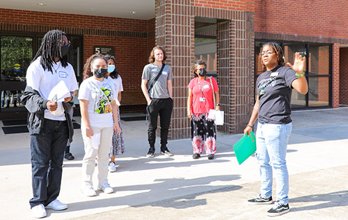 A small group of students listen to a person giving a campus tour