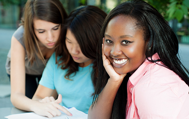 three high school students discuss classwork while one is smiling towards camera