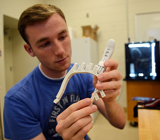 student inspects a 3D printed plastic finger recently added to a prosthesis 