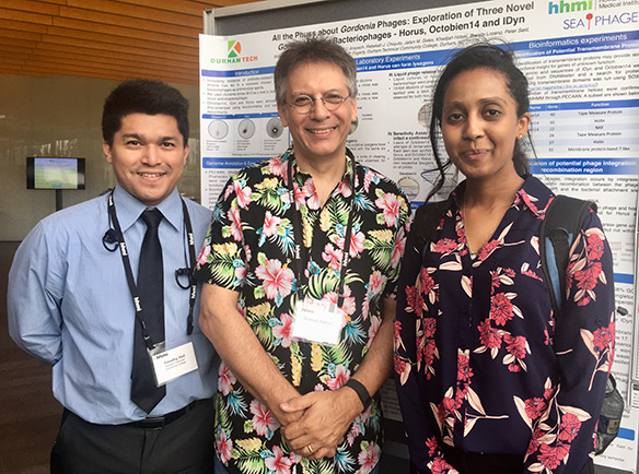 students Betiel Amanuel and Timothy Hall and scientist Graham Hatfull pose in front of poster 