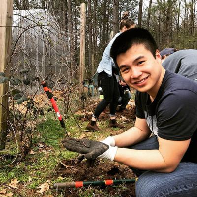 student holds worm in his gloved hand while working in the dirt at the community garden