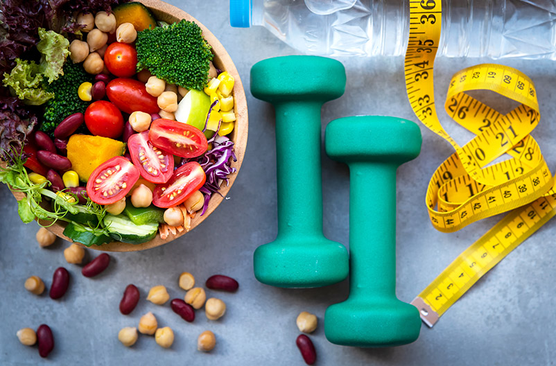 bowl of fruits and vegetables, scattered nuts, tape measure, hand weights