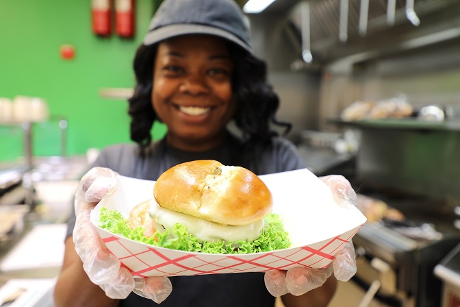 employee smiling and holding a hamburger in front