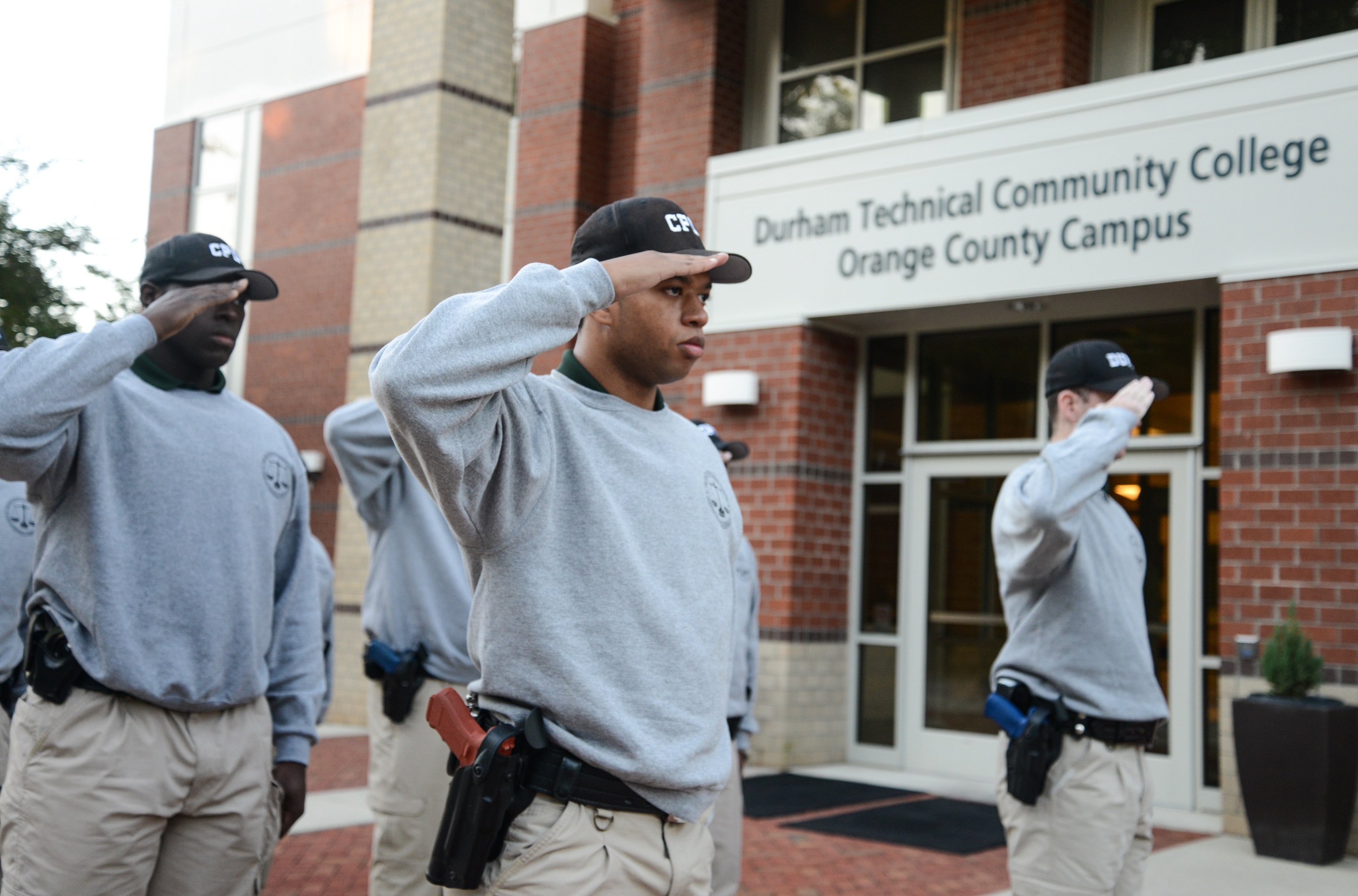 students saluting flag outside of orange county campus building