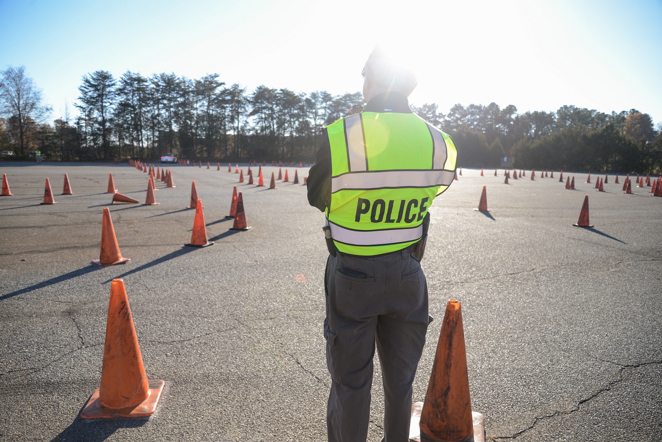 back of man with police vest standing in parking lot and orange cones throughout parking lot