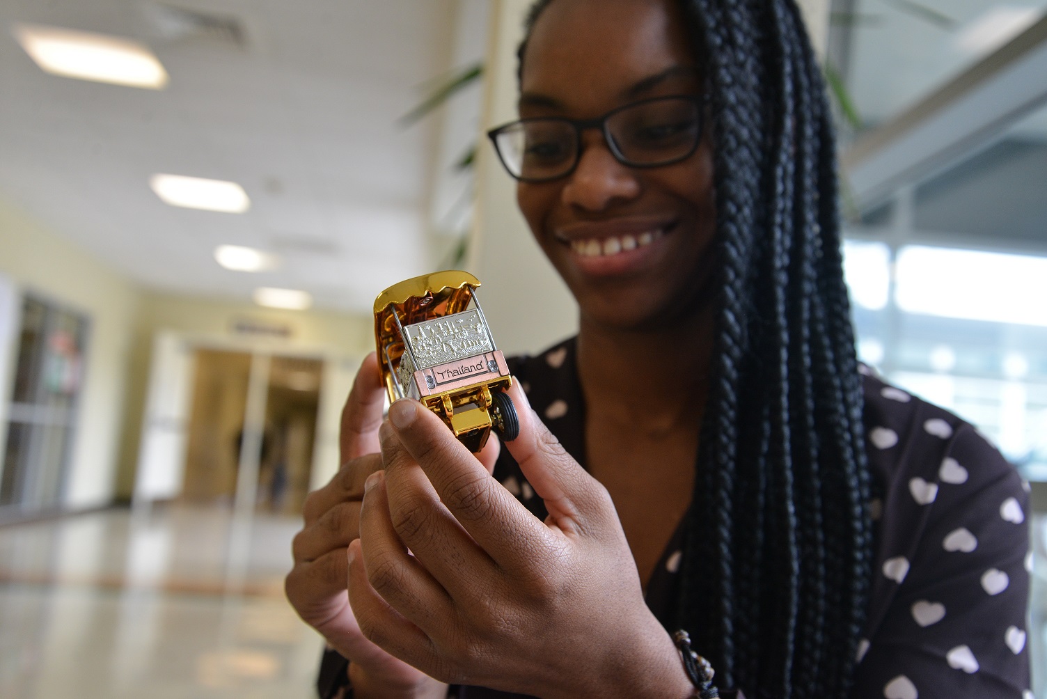 headshot of Jonitka sitting on chair in hallway of Durham Tech main campus, holding souvenier from Thailand, small car with Thailand written on back