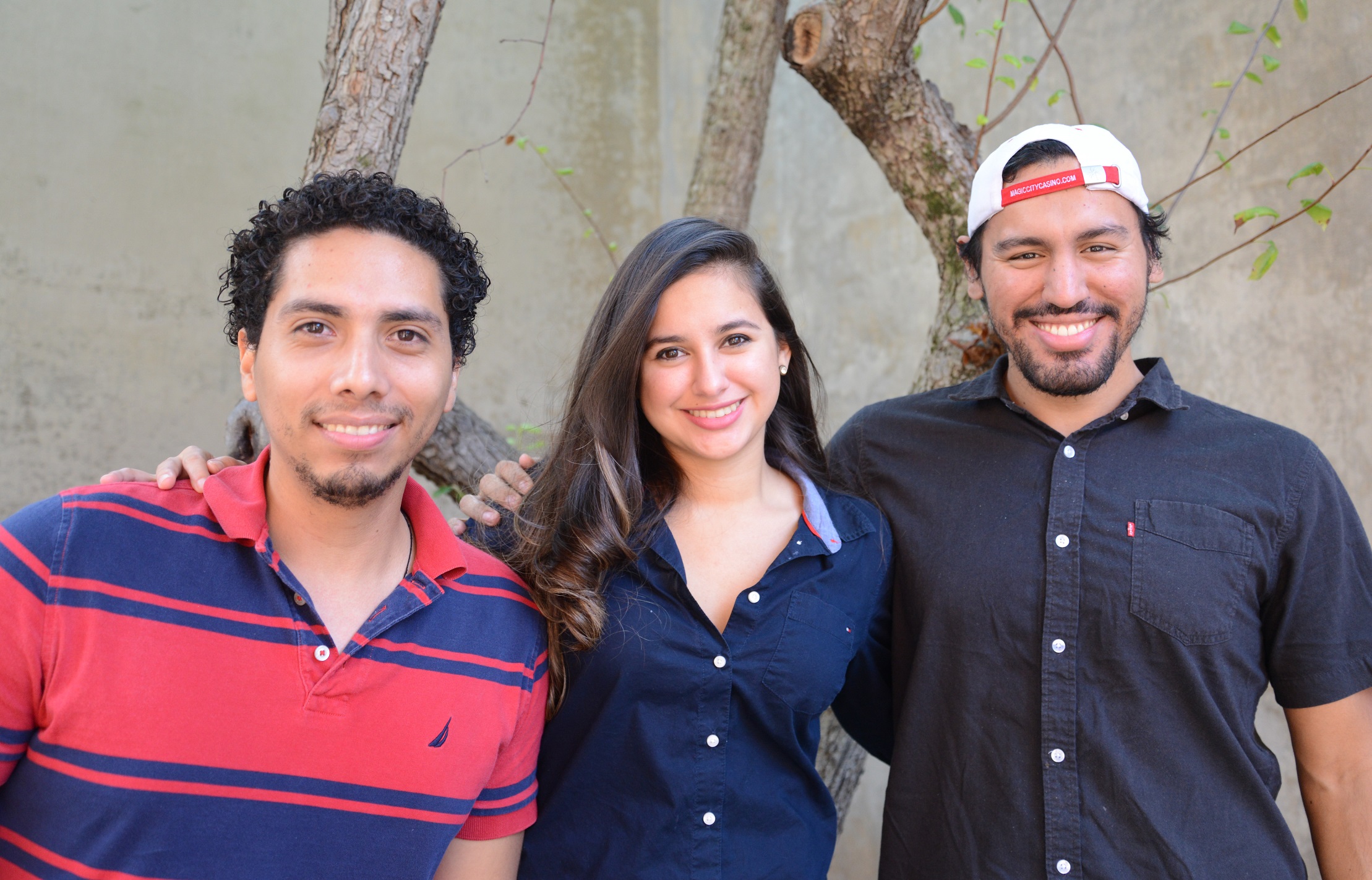 photo of three students smiling with tree behind them