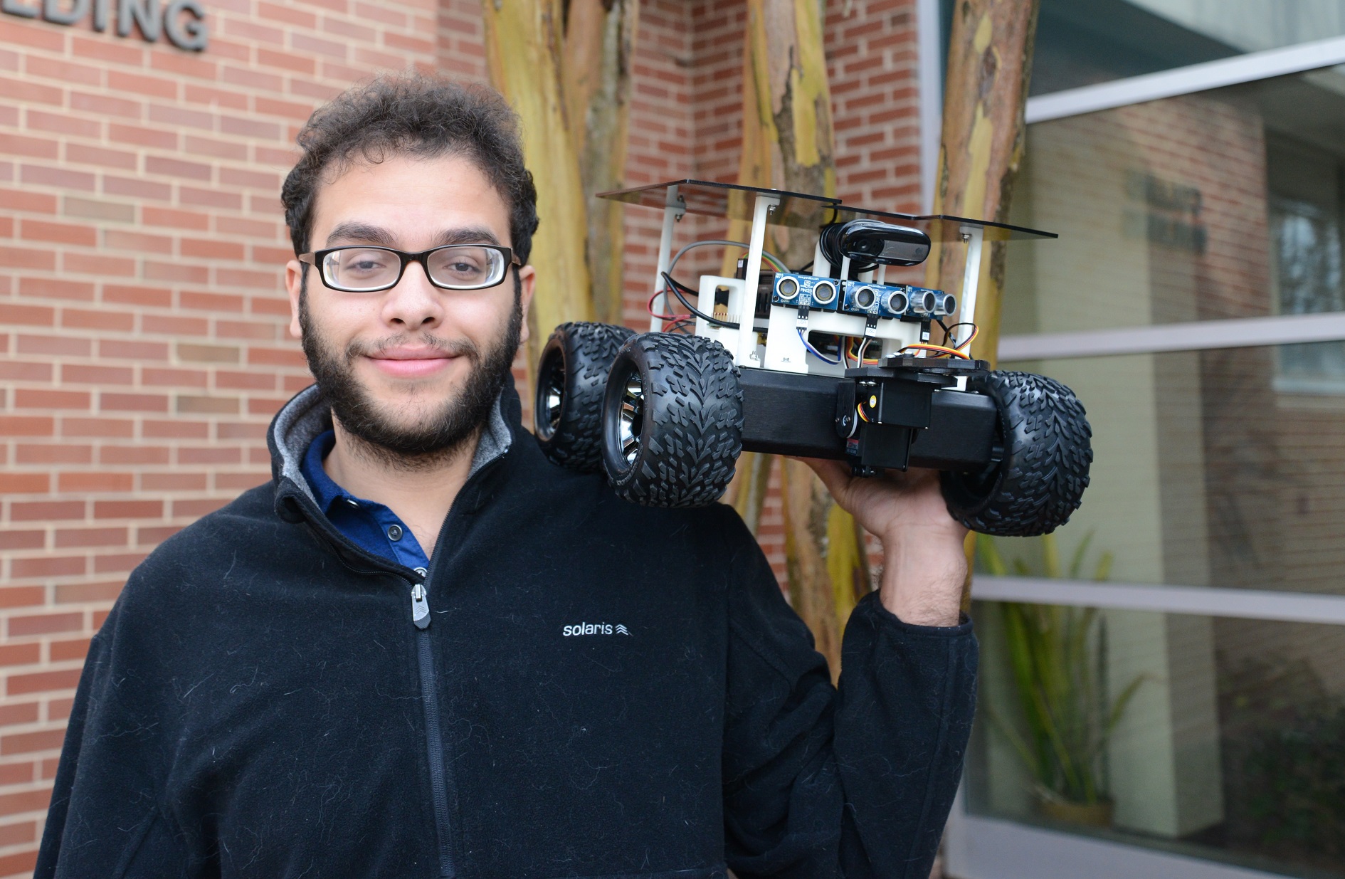 headshot of Mohamed standing in front of tree and holding up rover on his left shoulder