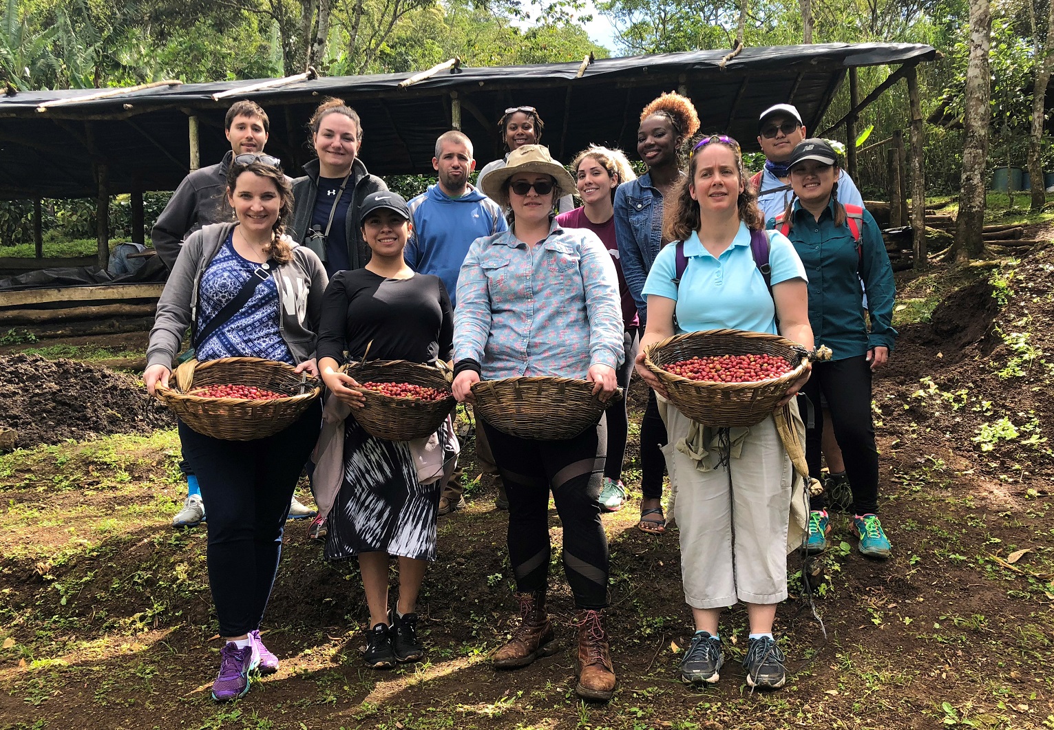 Group photo of students holding baskets of coffee beans on coffee farm