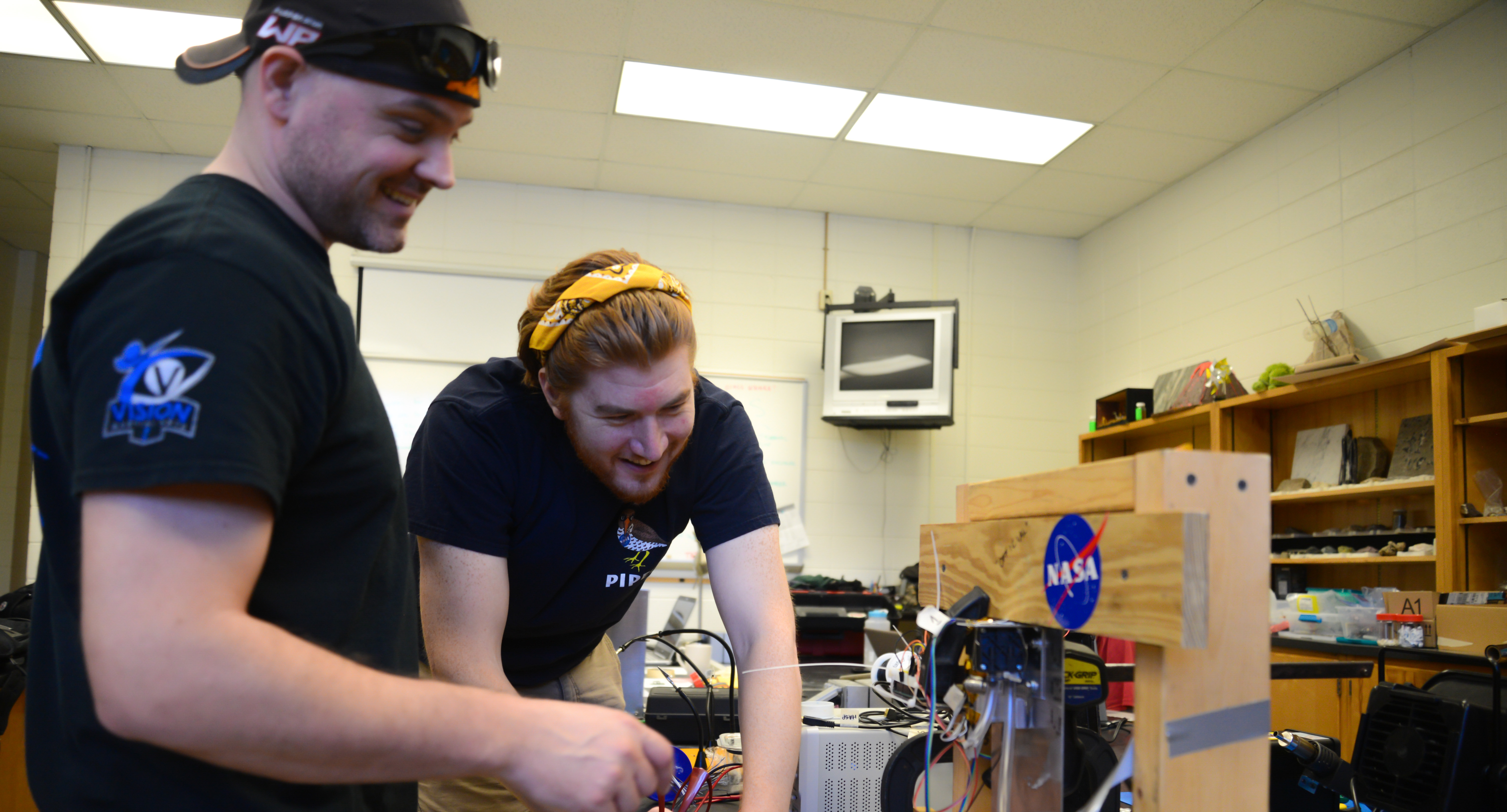 two students leaning over table looking at gadet with NASA sticker