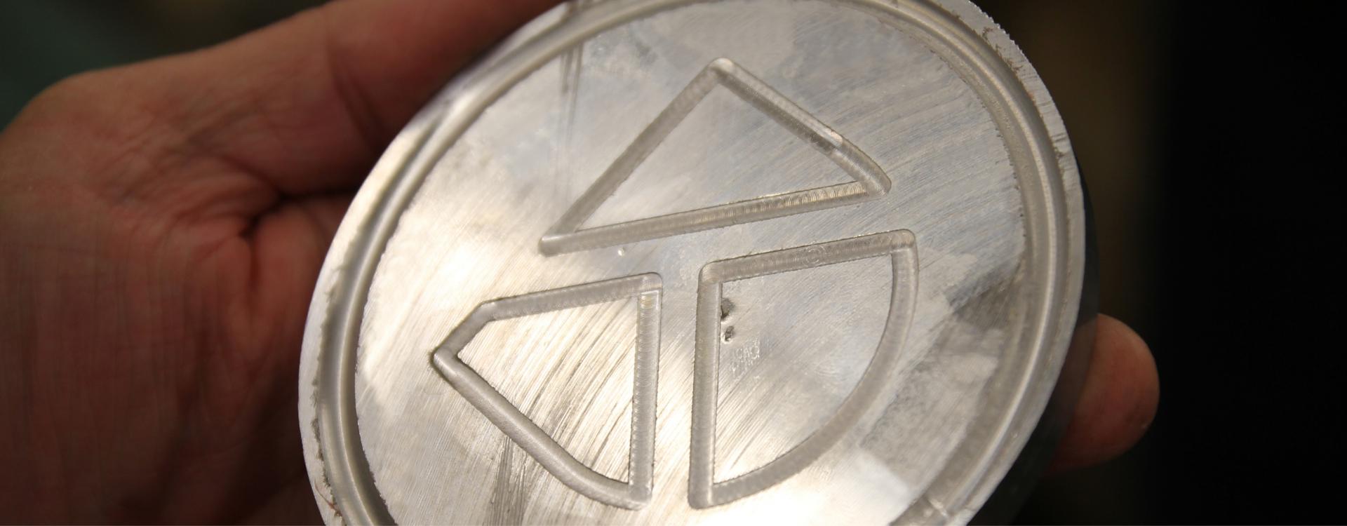 Close up photo of a silver circle piece of metal with Durham Tech's logo that was made by machining students