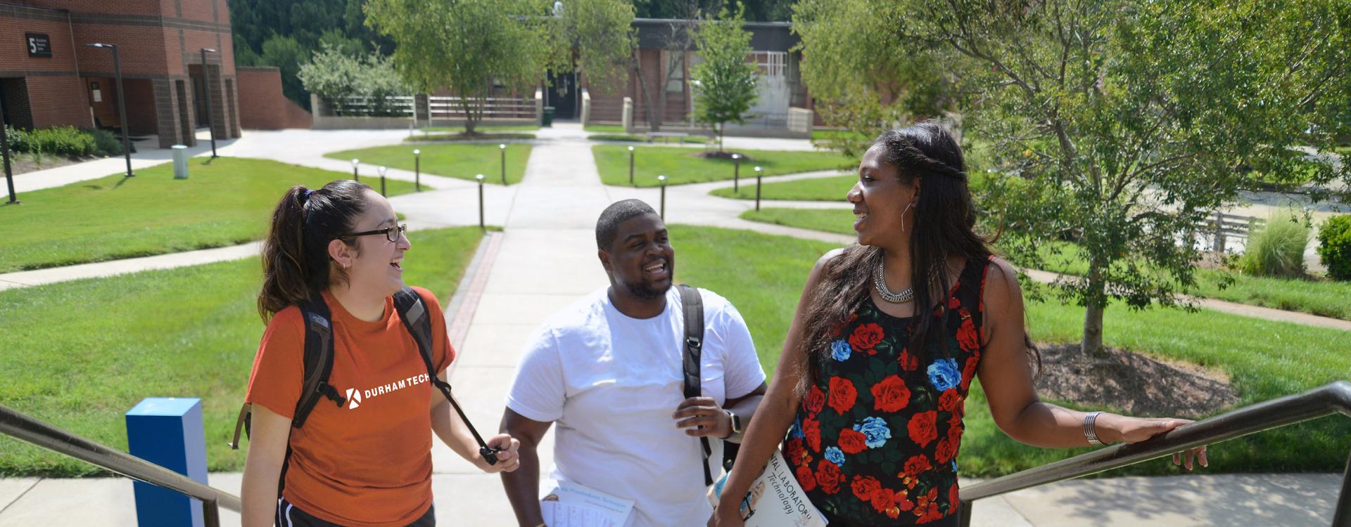 three smiling students walking up outddor stairs on main campus