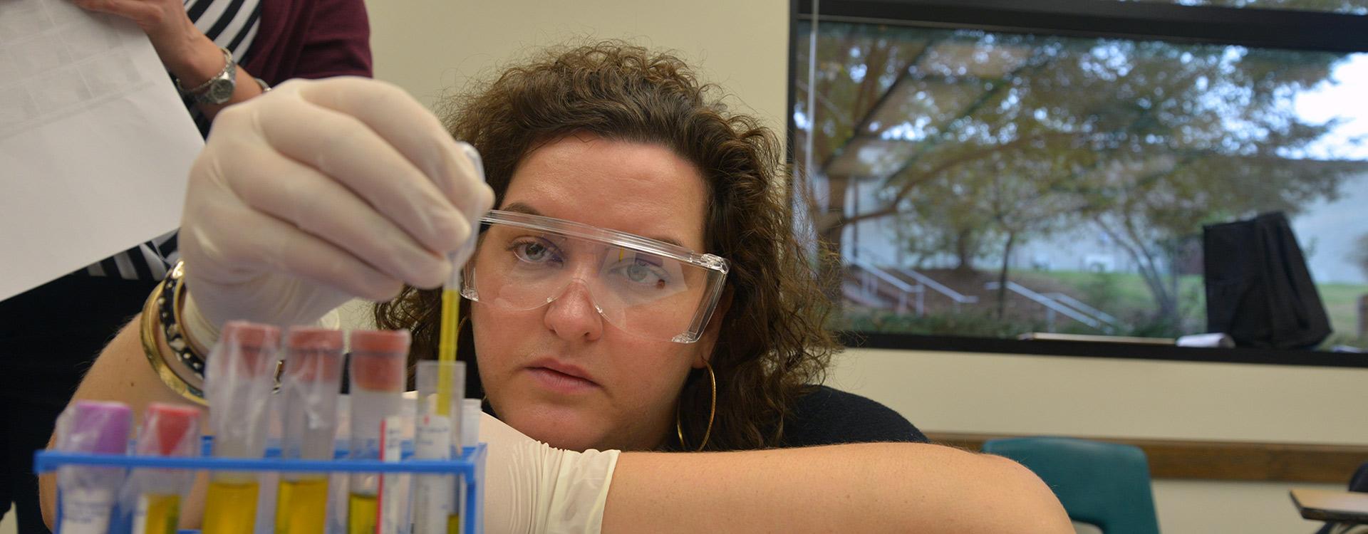 clinical trials student is using a pipette to extract fluid from a test tube
