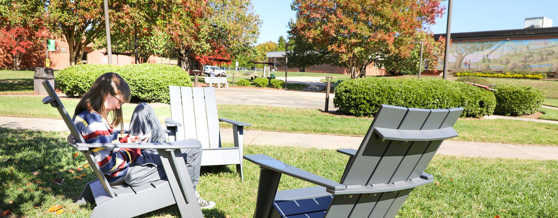 student sitting in the Main Campus Plaza in Andirondack chair on a fall day