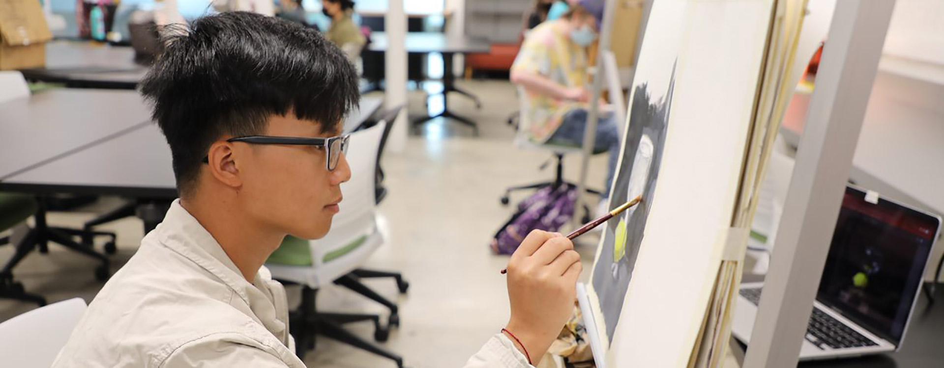 student painting artwork on an easel in fine arts class