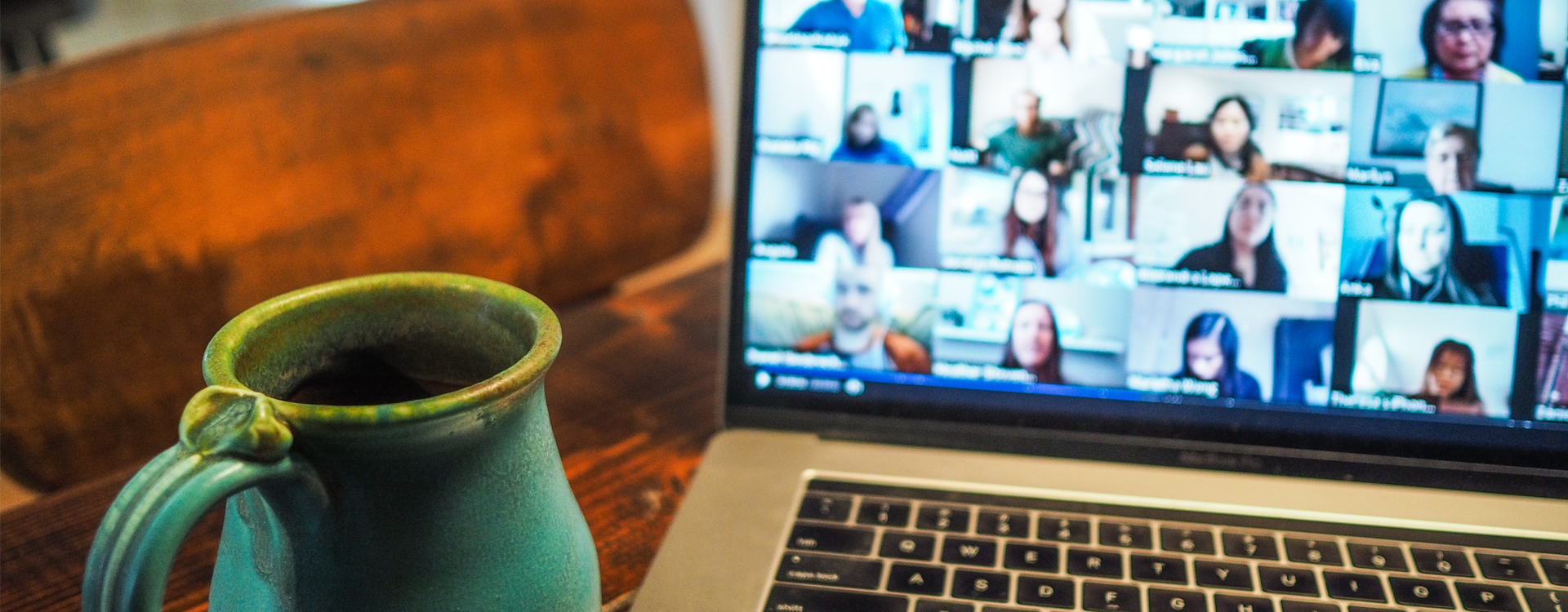 coffee cup next to a laptop with images of people in an online meeting