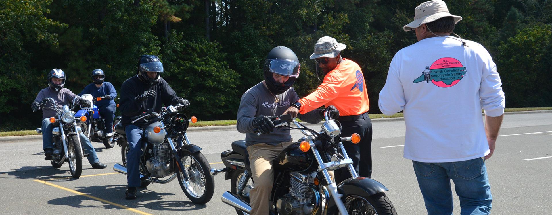 students ride motorcycles in a line as the instructor watches