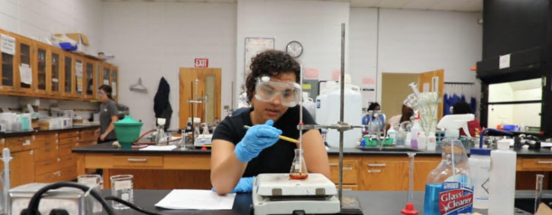 student wearing protective goggles in chemistry lab working with glass titration apparatus