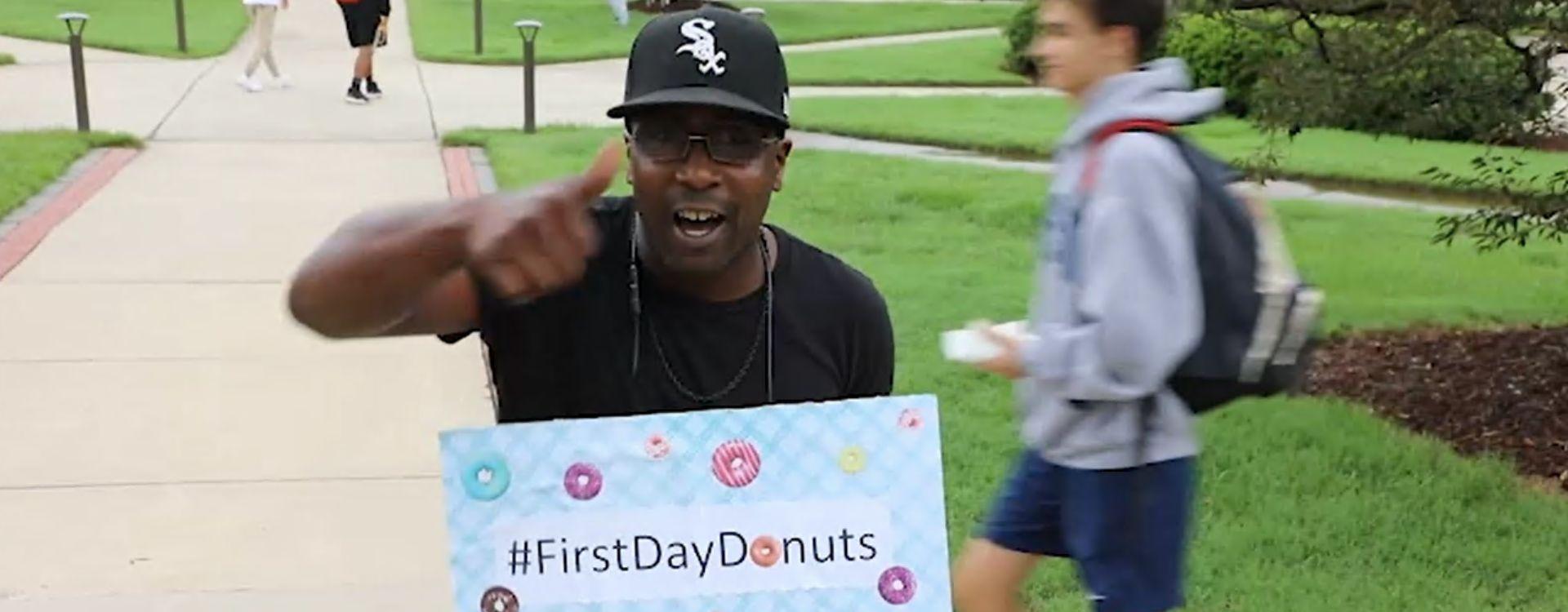 Student with their thumb raised holding a sign with the hashtag #firstdaydonuts