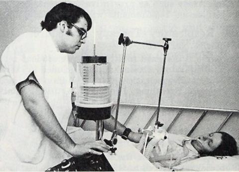 1973 inhalation therapy student in lab practicing with "patient" using an old-fashioned looking respiration device