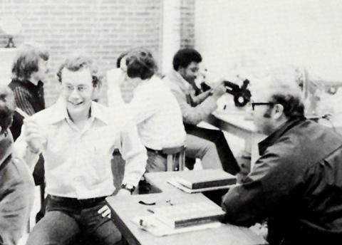 1973 opticianry lab with several students practicing with equipment and laughing and talking