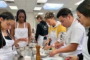 high school students wearing aprons and chopping vegetables