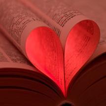 Shows an open book with a few pages tucked back into the spine to form the shape of a heart.