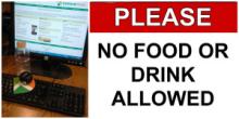 A photograph focusing on a keyboard and computer monitor with a plum and water bottle. Text says, "Please no food or drink allowed"