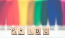 PRIDE Scrabble letters on a faded rainbow background
