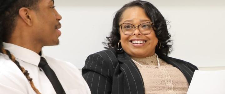 A student wearing a dress shirt and tie speaking with their teacher during a mock business interview