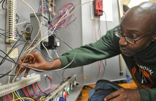 adult male student inserts wire into electrical board 