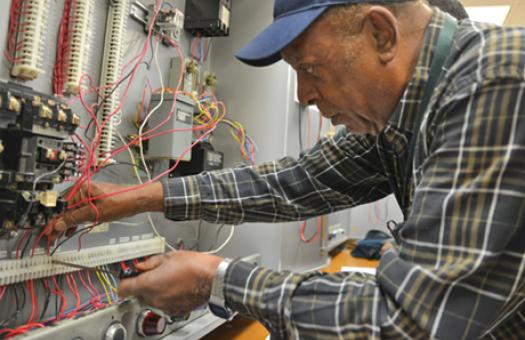 older male student screws wires into electrical board 