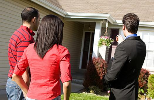 real estate agent and a couple stand in front of a home for a showing