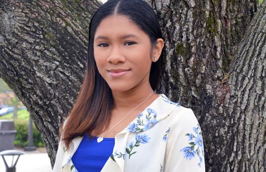 Student smiling in front of tree on main campus. 