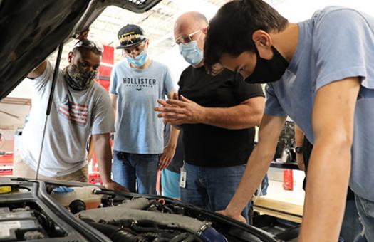masked instructor and students look at auto engine in automotive lab